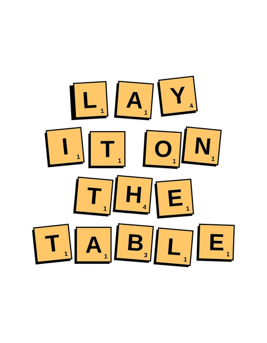 Scrabble betűkkel formázott "LAY IT ON THE TABLE" szöveg látható, ami a nyíltságot és őszinteséget hangsúlyozza. 